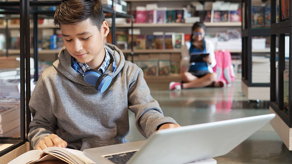 A young student sits with a laptop and book