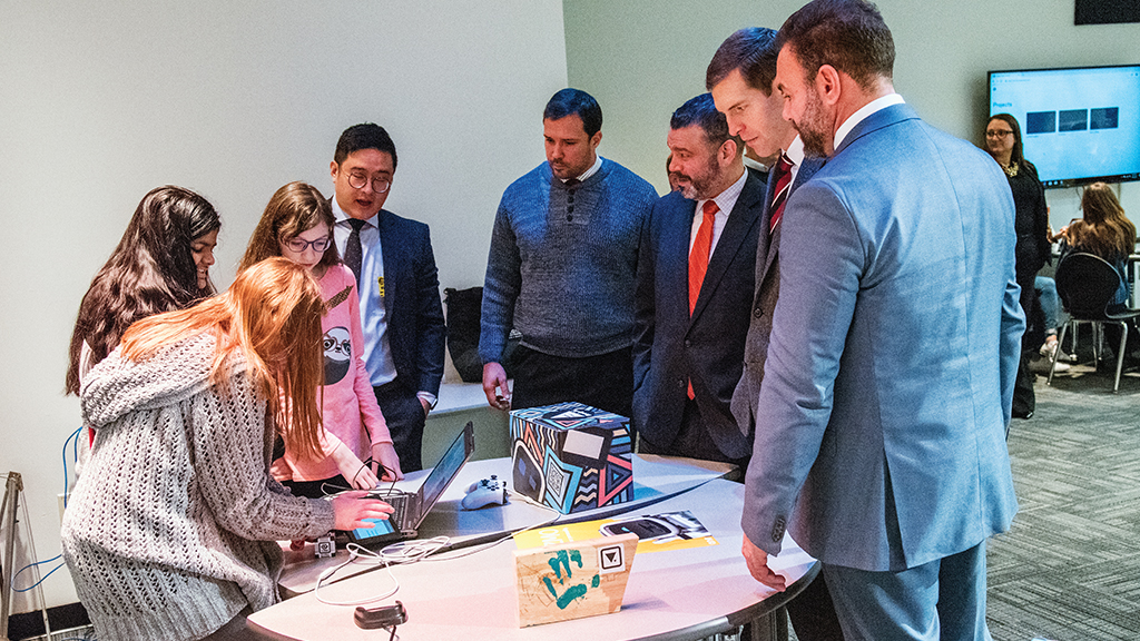 A student shows her work to several politicians and education leaders