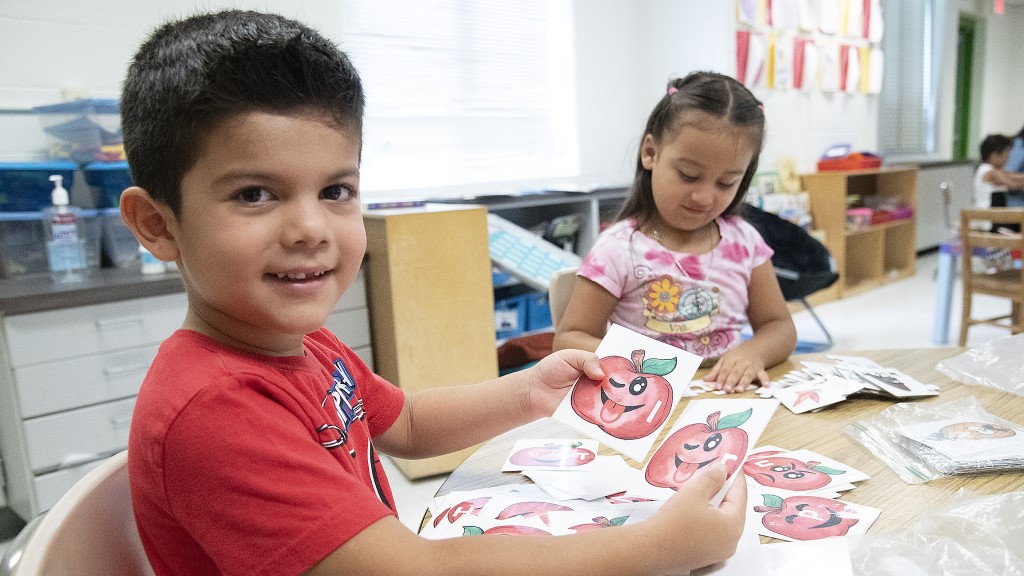 A boy smiles and shows the camera his work