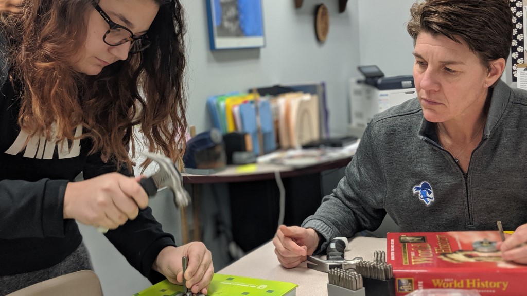 a student uses a hammer as a teacher observes