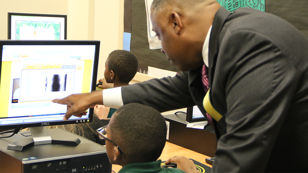 rodney jordan looks over a student working on a desktop computer and points to the screen