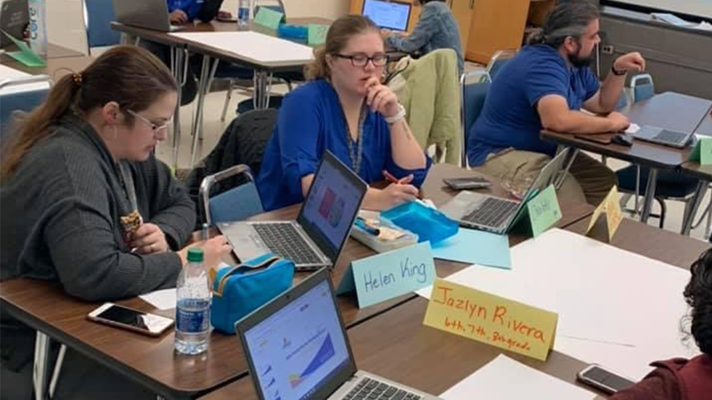 a group of teachers gathered around on desks and doing work