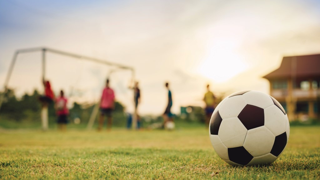 a soccer ball on a field in the foreground. in the background, students are playing