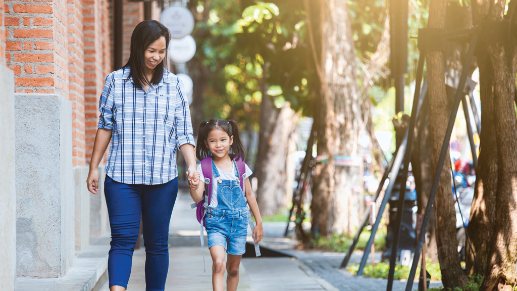 an asian american woman holds hands with her daughter as they walk to school