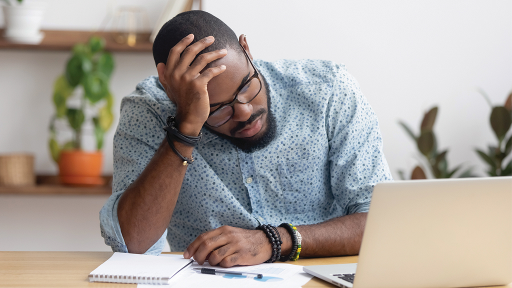 a teacher has his head in his hands as he looks at a laptop