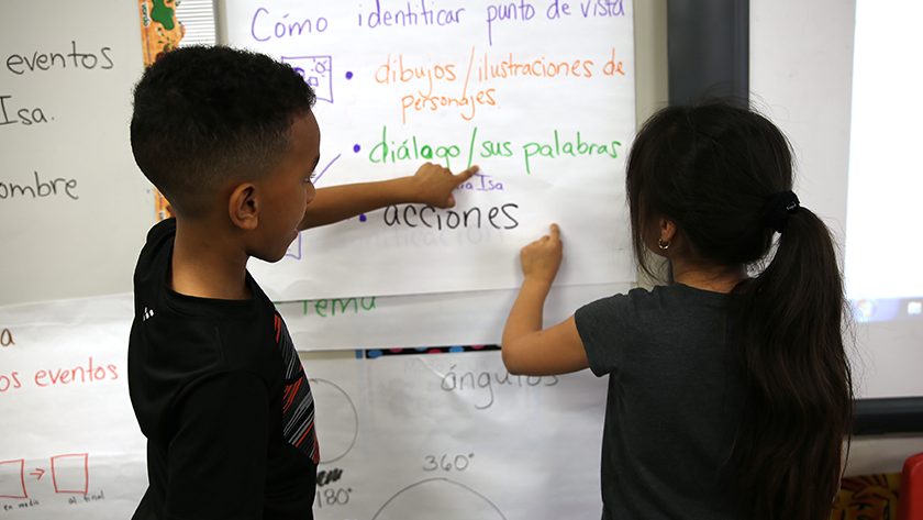 Two students look at words written on a wall chart