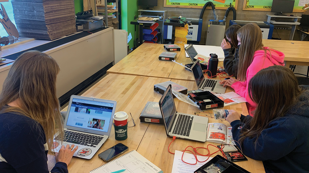 Three high school students work on laptops at a table