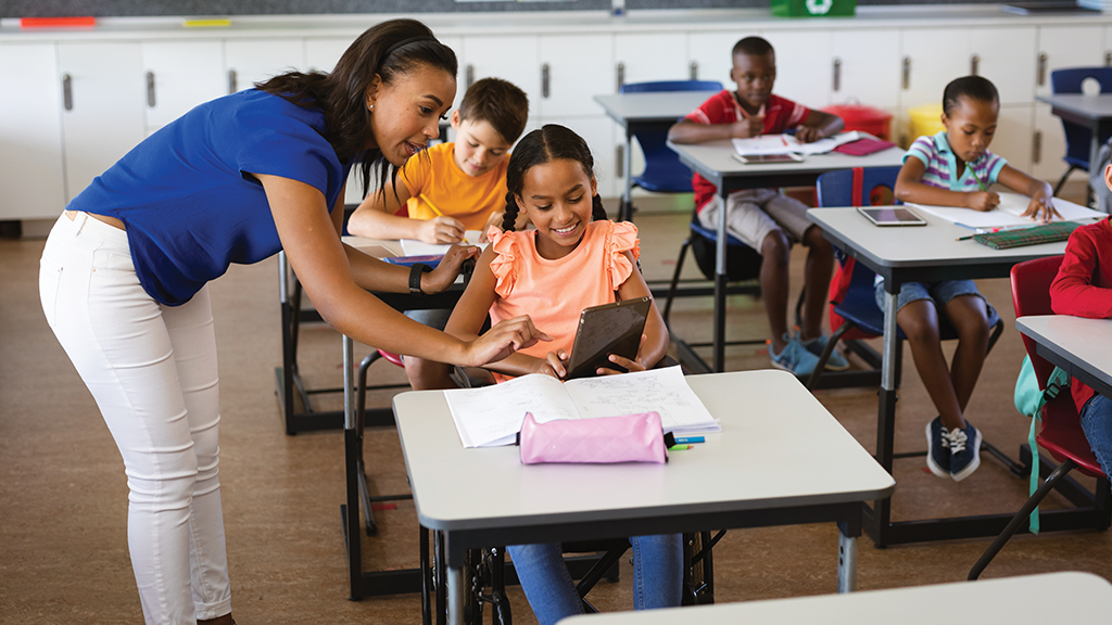 An elementary school teacher looks at a student's work on an iPad