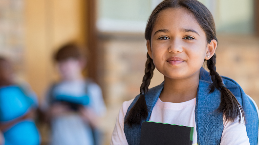 An elementary school girl with long braids holds her school books