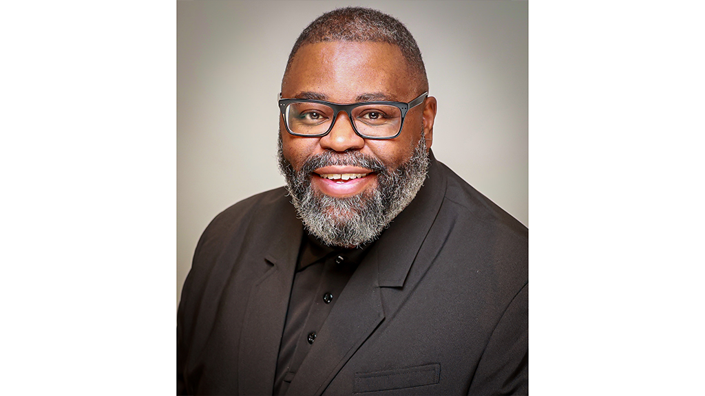 A man with a beard and eyeglasses smiles at the camera. 