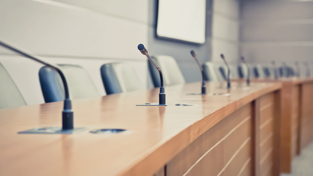 a series of microphones are positioned atop a long desk 