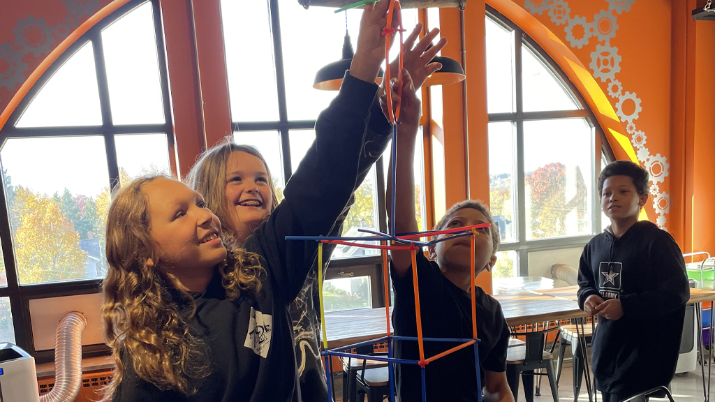 Young girls stretch their arms to reach the top of their new creation. 