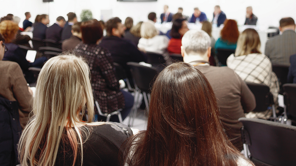 A group of adults watch a board meeting