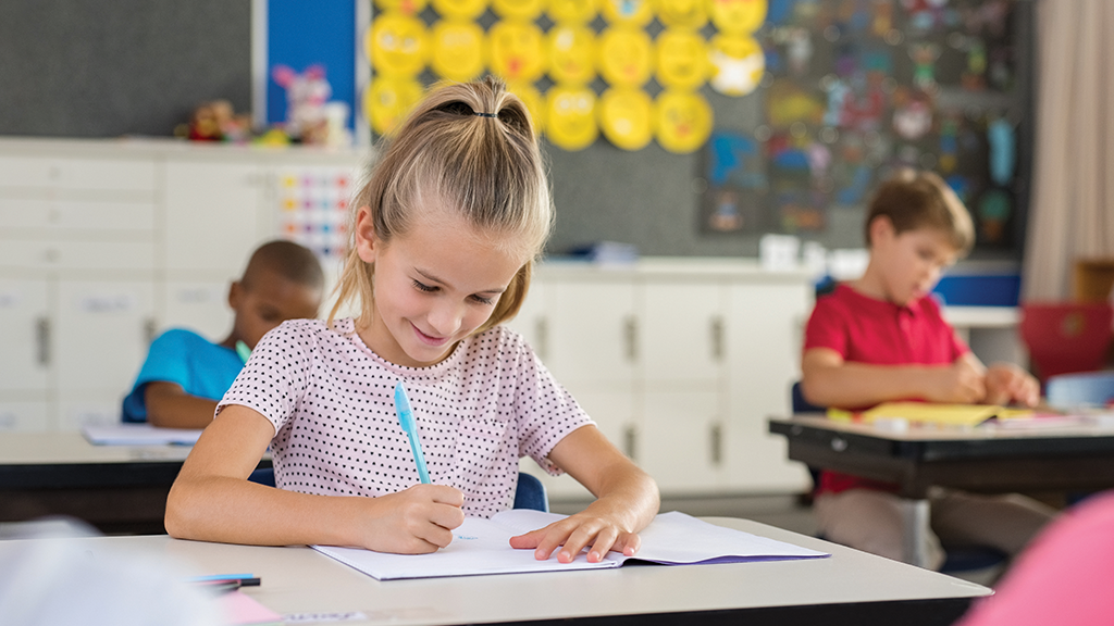 a young girl writes in a booklet with a blue pen