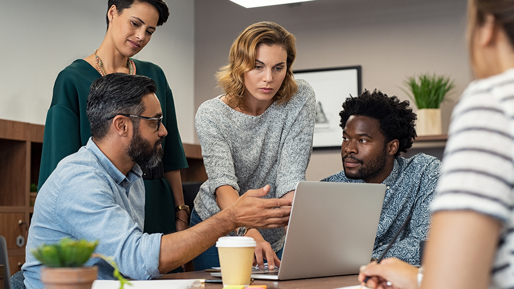 A group of adults look at a laptop and engage in a conversation.