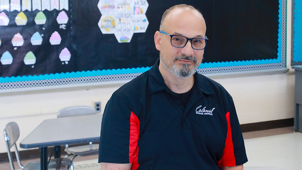 Jon Cooper, director of health and wellness for Delaware’s Colonial School District, sits on a desk in a second-grade classroom at Eisenberg Elementary. 