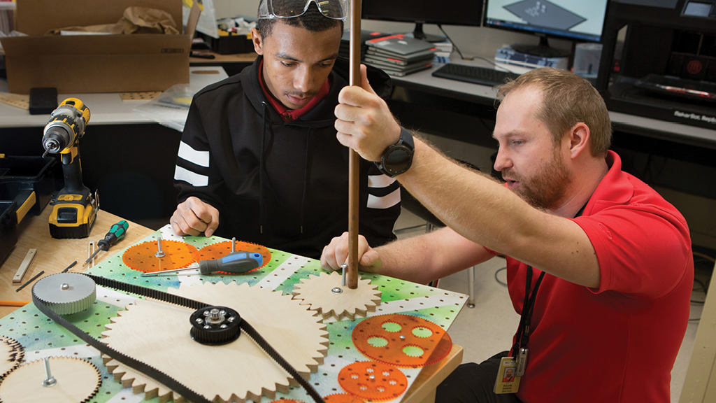 A teacher and a high school student use a screwdriver to tighten up a group of pulleys.