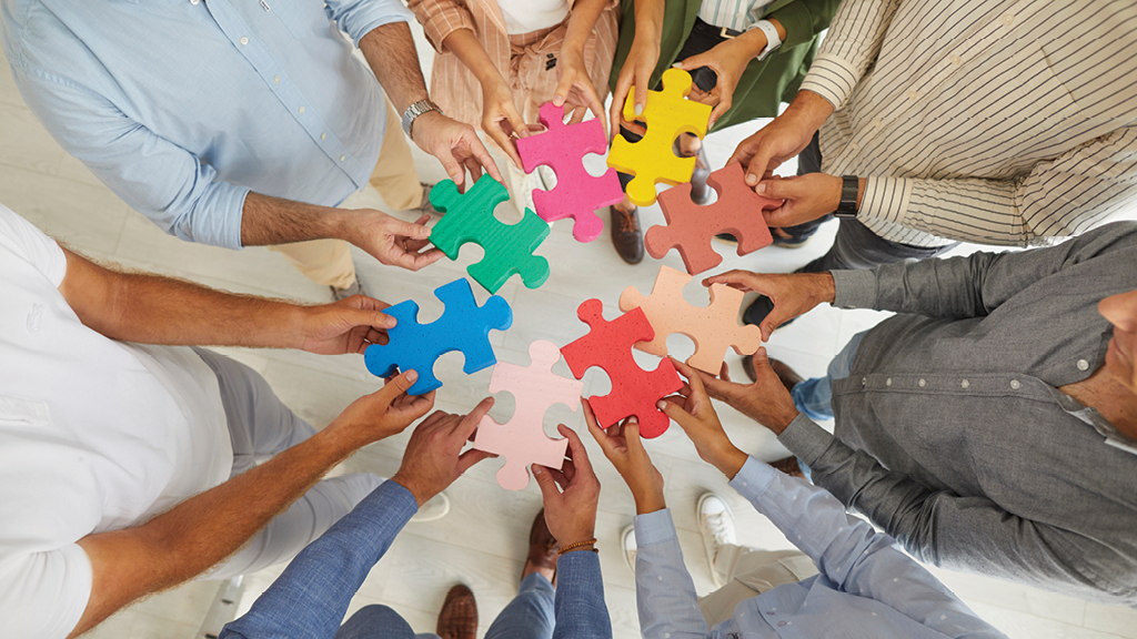 a group of adults stand in a  circle and each one holds a piece of a puzzle.