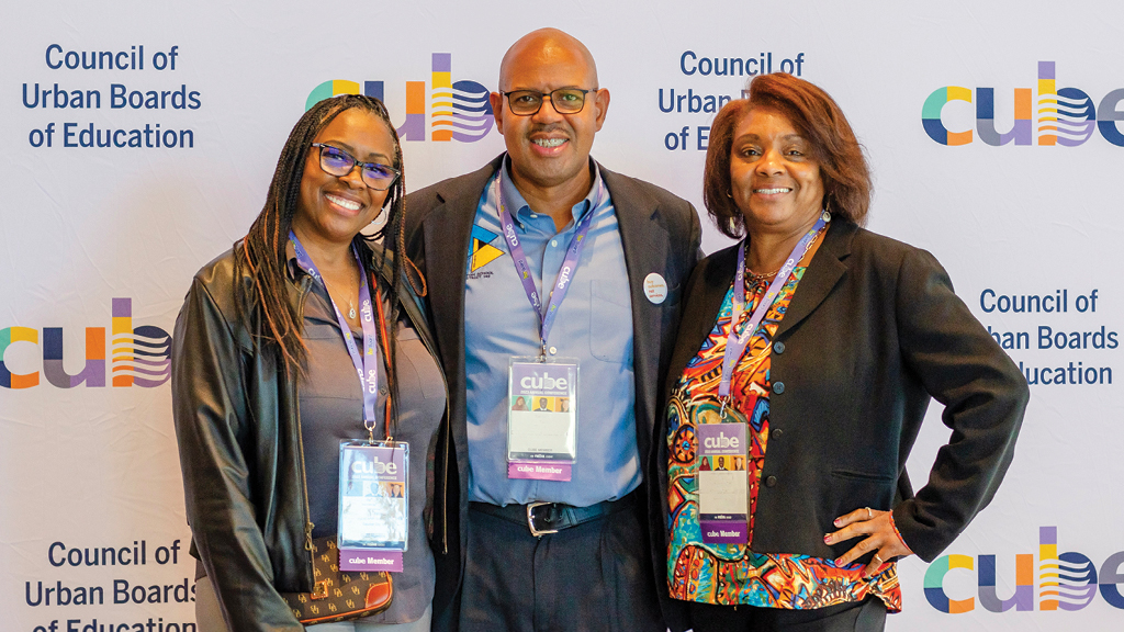 three adults wearing conference lanyards around their necks smile at the camera. 