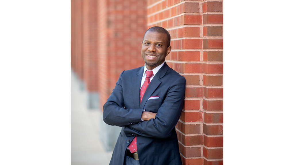 ivory toldson smiles while leaning against a brick wall