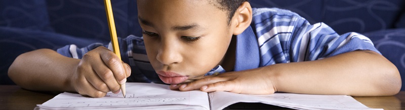 a boy with a frustrated expression writes in a notebook